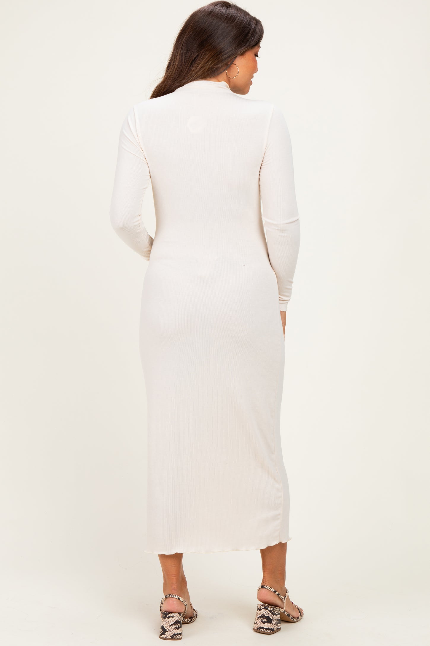 woman wearing a light beige long sleeve maternity dress, showing a fitted silhouette from the back