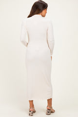 woman wearing a light beige long sleeve maternity dress, showing a fitted silhouette from the back