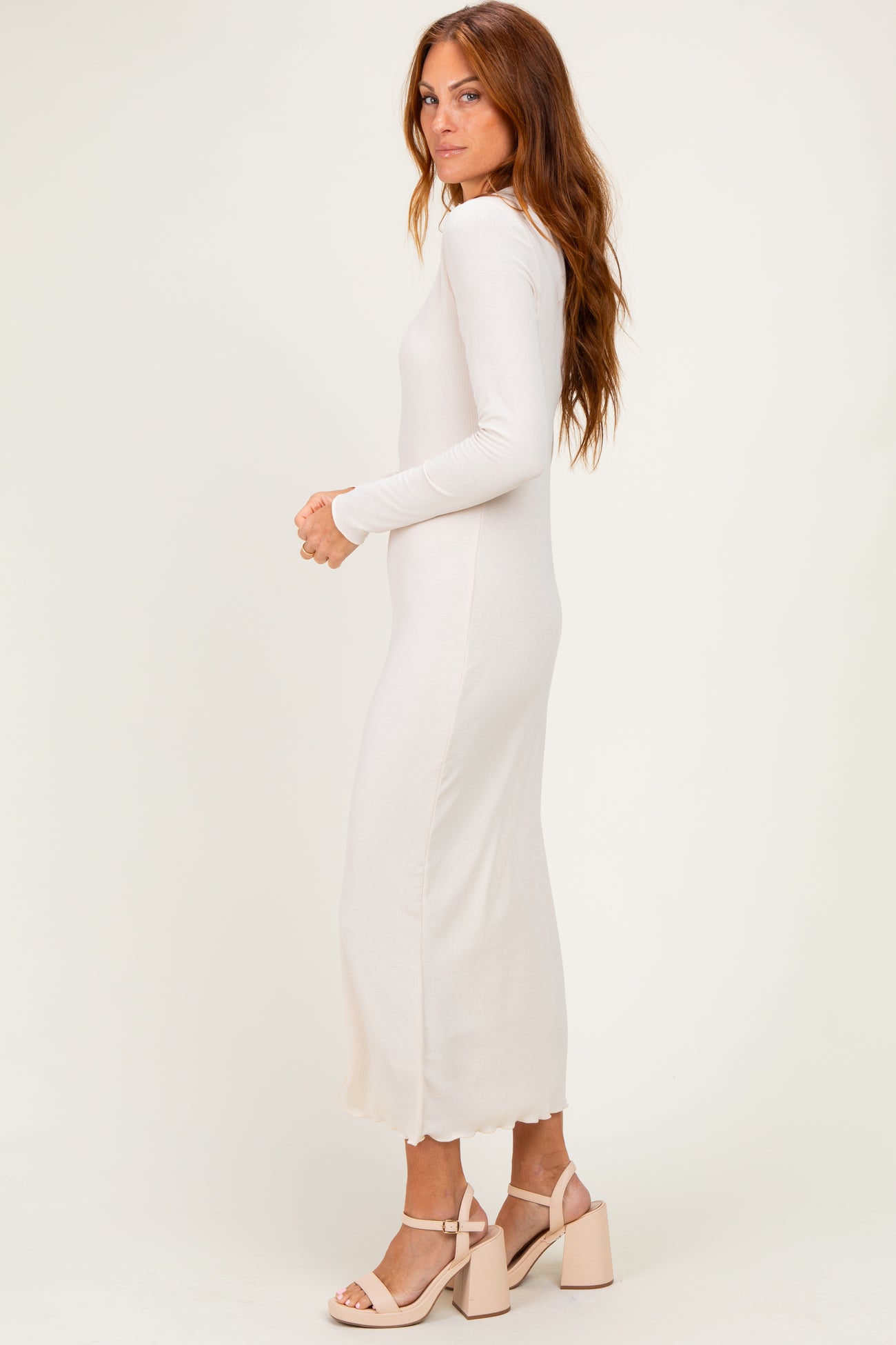 woman wearing a cream long sleeve midi dress with a scalloped hem and paired with heeled sandals