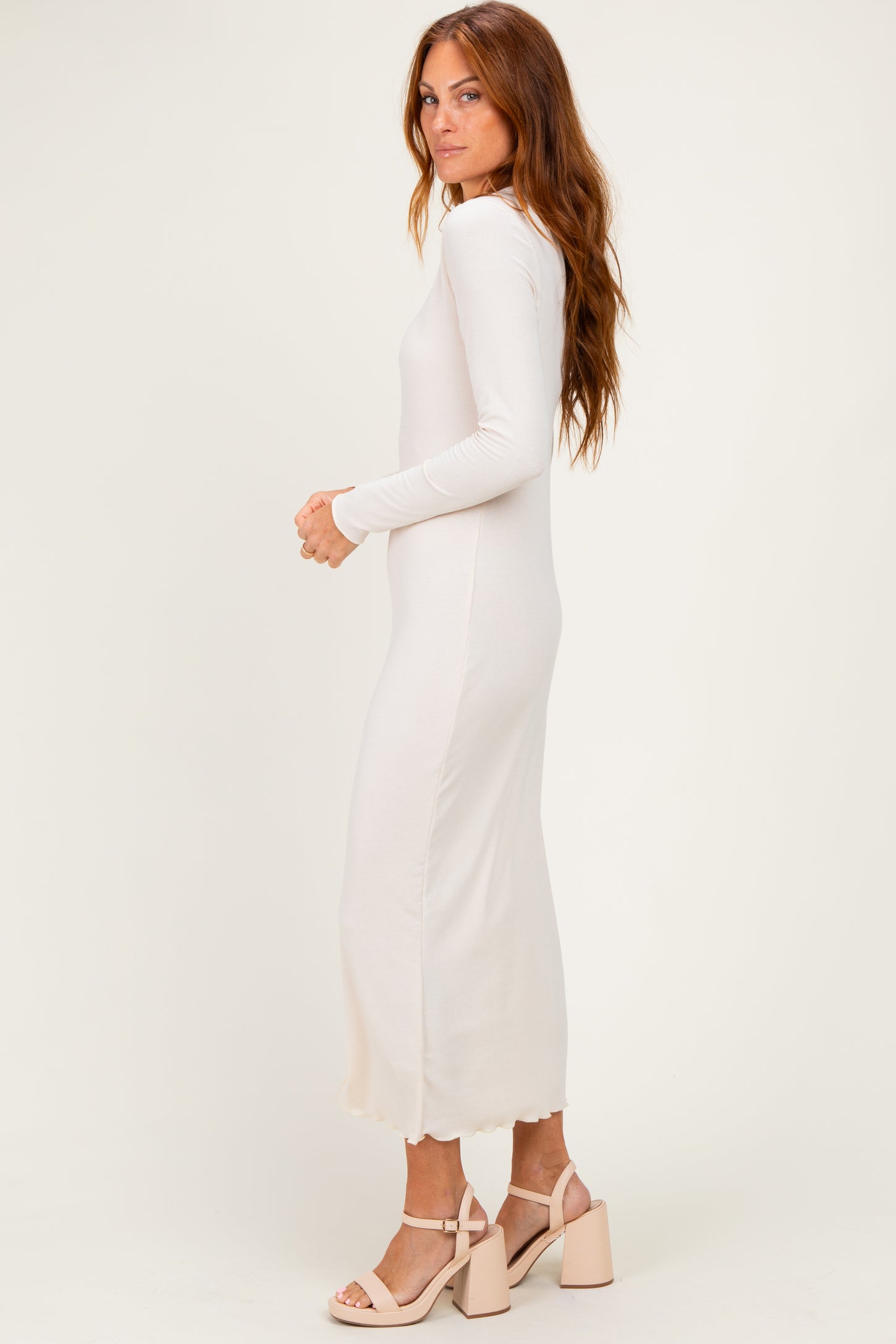 woman wearing a cream long sleeve midi dress with a scalloped hem and paired with heeled sandals