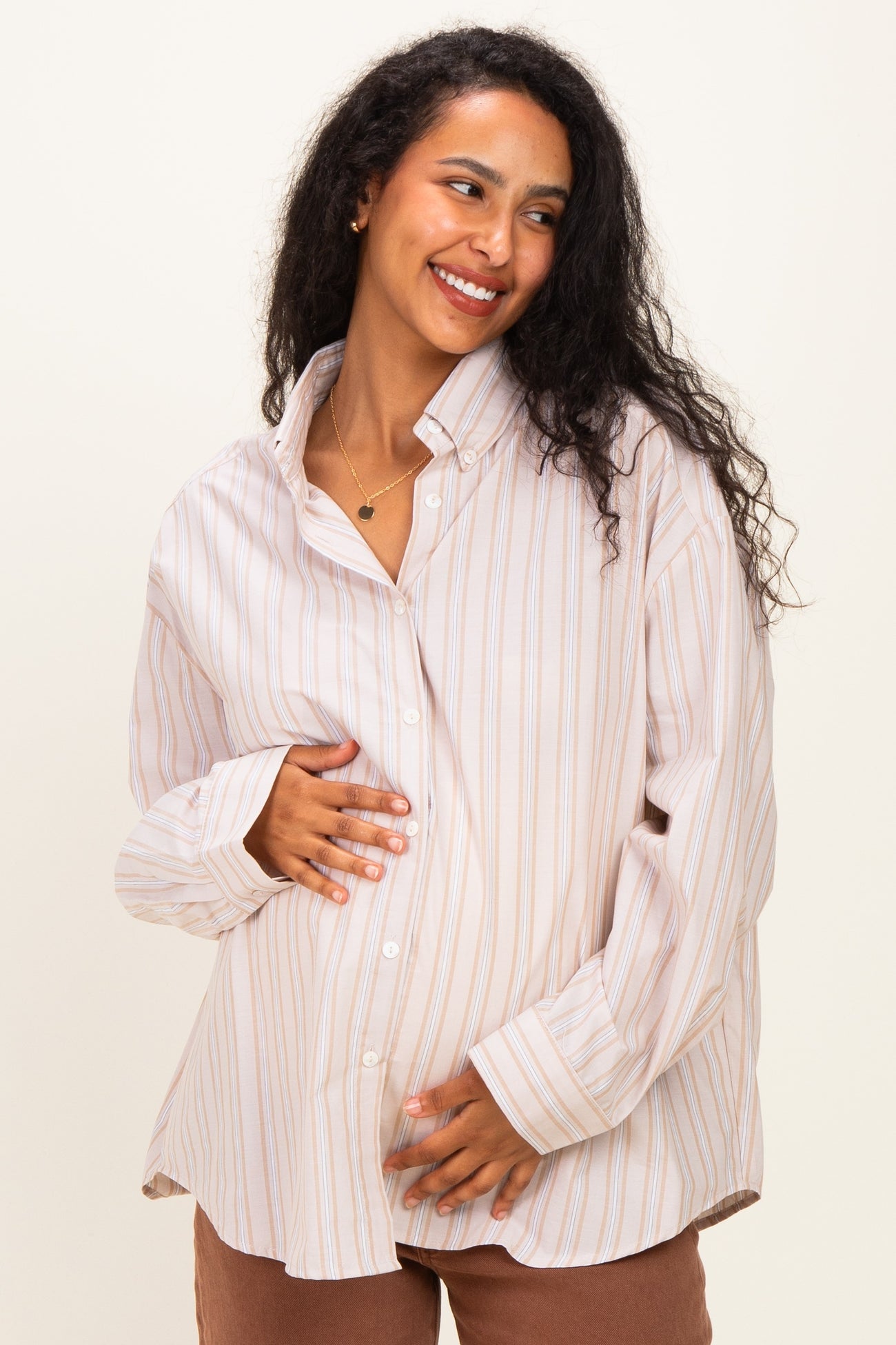 woman wearing a cream and pastel striped maternity button-up shirt and holding her baby bump