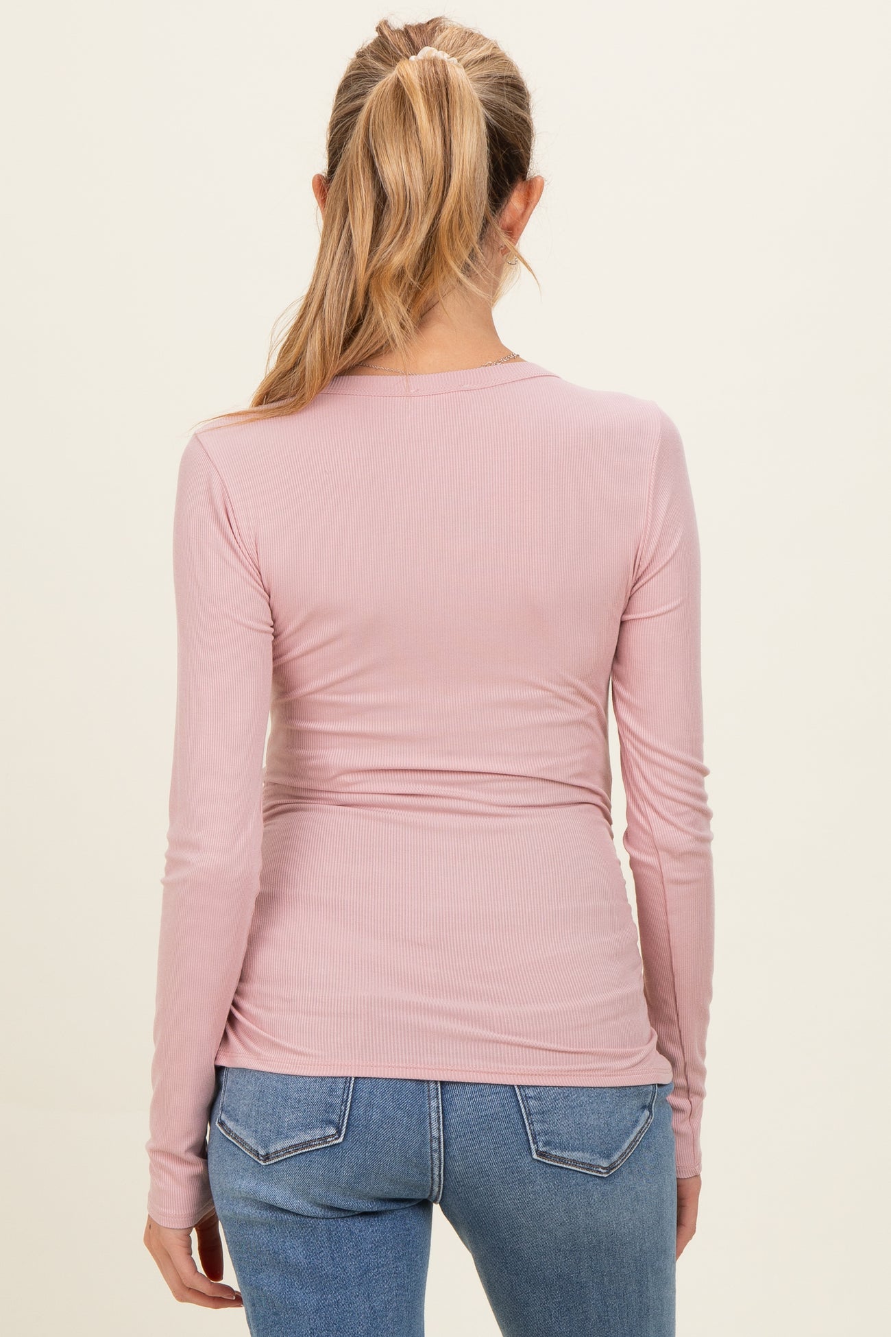 woman wearing a light pink long sleeve maternity top with a fitted style and visible ruching at the back
