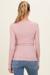 woman wearing a light pink long sleeve maternity top with a fitted style and visible ruching at the back