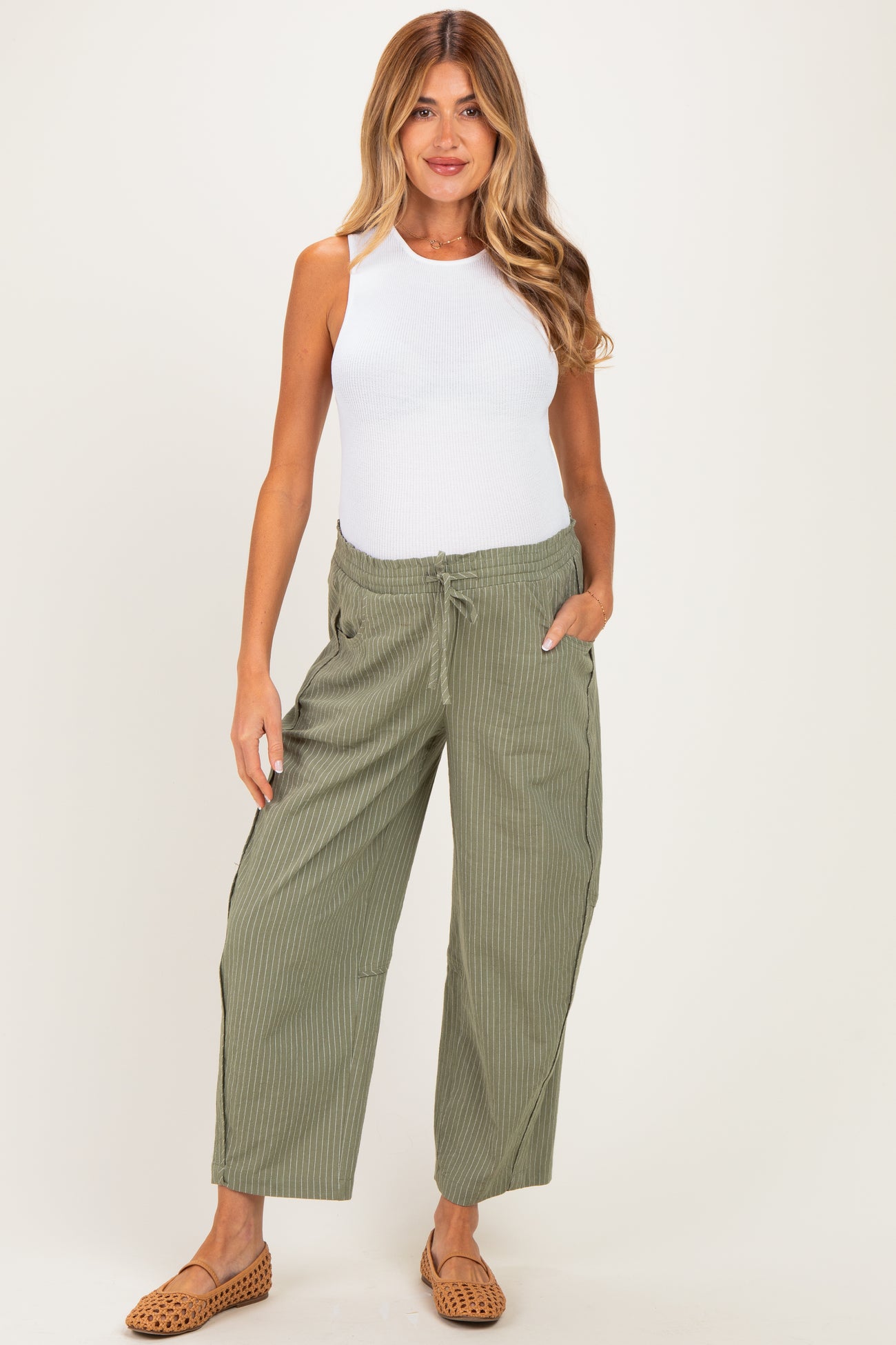 woman wearing a white tank top and green striped maternity pants with pockets and drawstring waist
