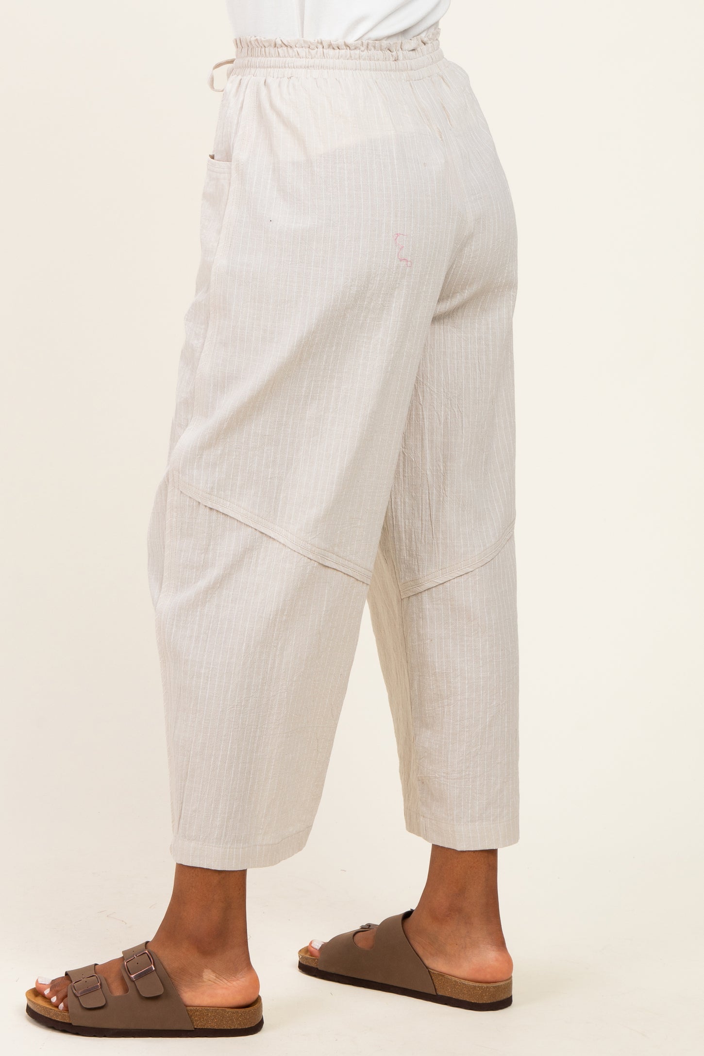 woman wearing light beige wide-leg pants with an elastic waistband and side pockets, paired with brown slide sandals