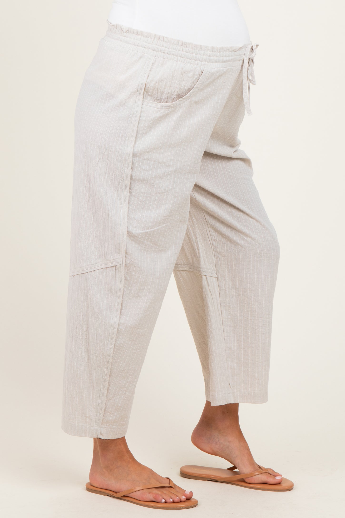 woman wearing light beige maternity pants with pockets and an elastic waistband, standing in a relaxed pose