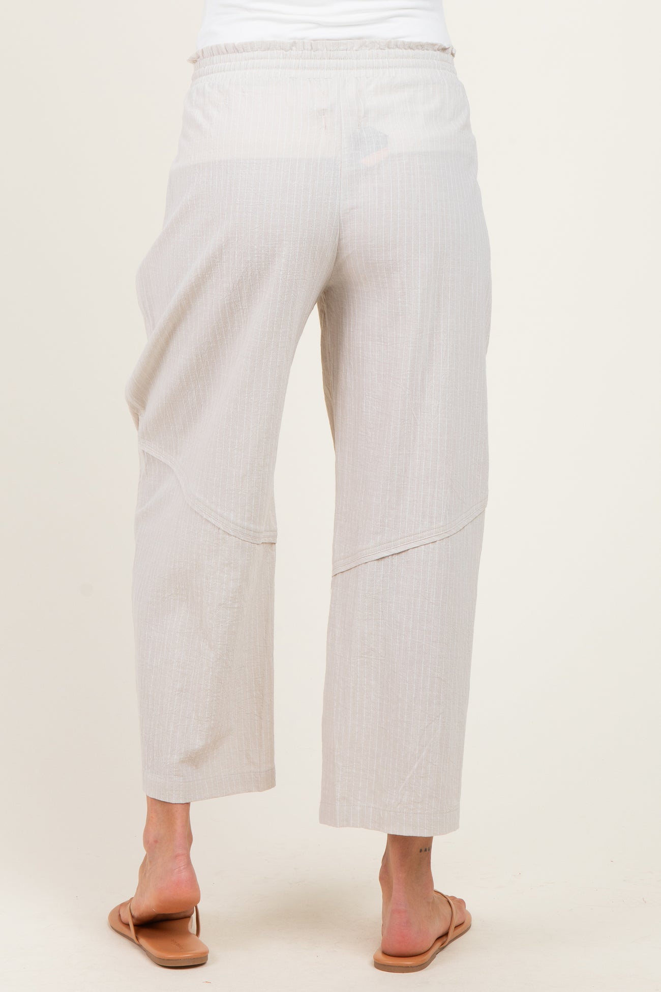 woman wearing light beige maternity pants with a relaxed fit and elastic waistband, viewed from the back