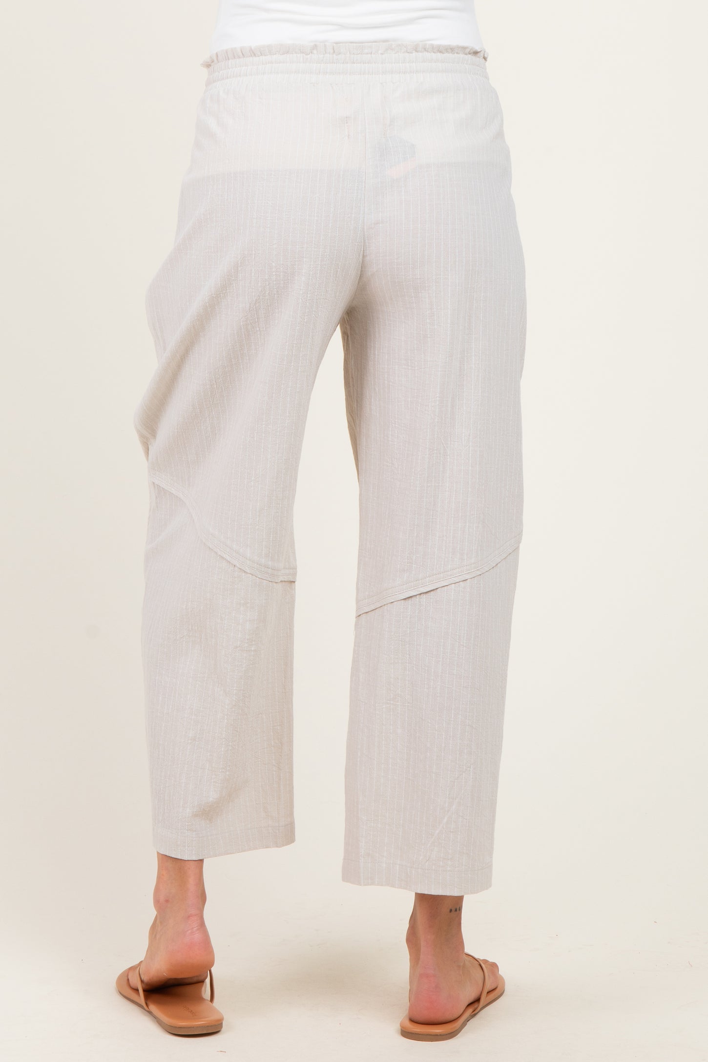 woman wearing light beige maternity pants with a relaxed fit and elastic waistband, viewed from the back