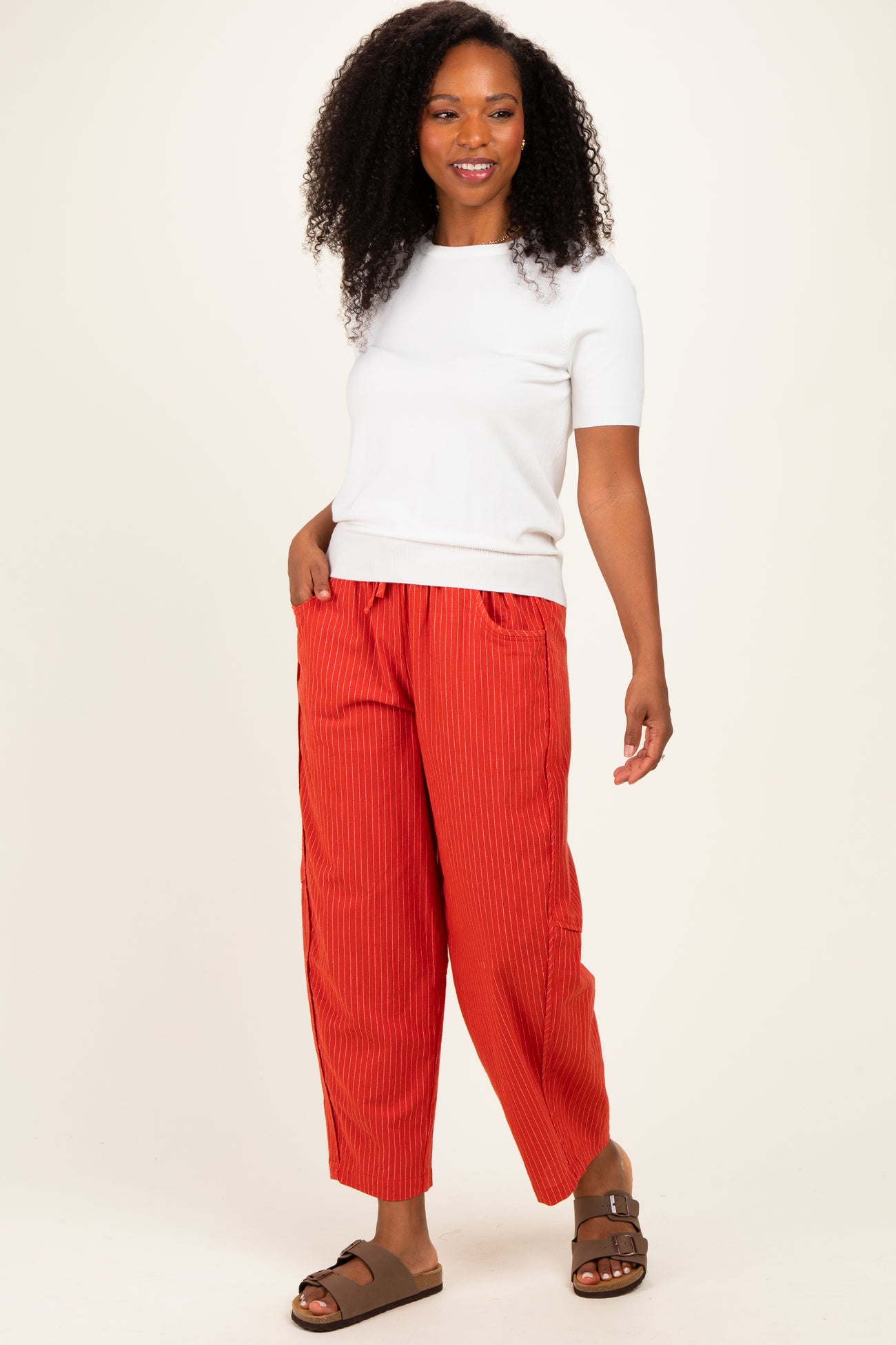 woman wearing a white short sleeve top and orange ribbed wide-leg pants, smiling and facing forward
