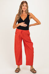 woman wearing a black maternity tank top and rust-colored wide-leg maternity pants, holding her baby bump