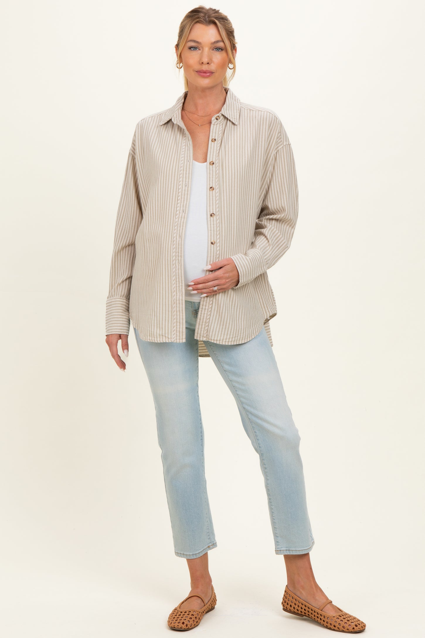 woman wearing a beige striped maternity button-up shirt and light blue jeans, showing her baby bump