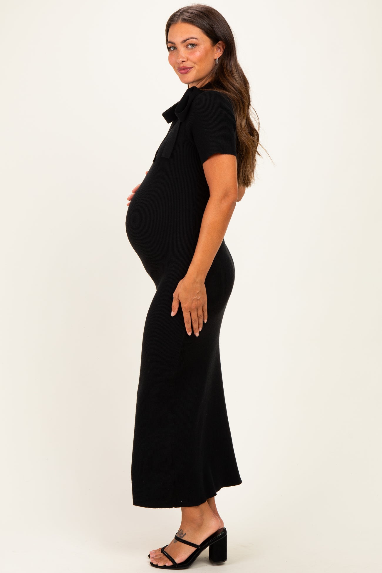 woman wearing a black ribbed maternity dress with a bow detail, showcasing her baby bump from the side