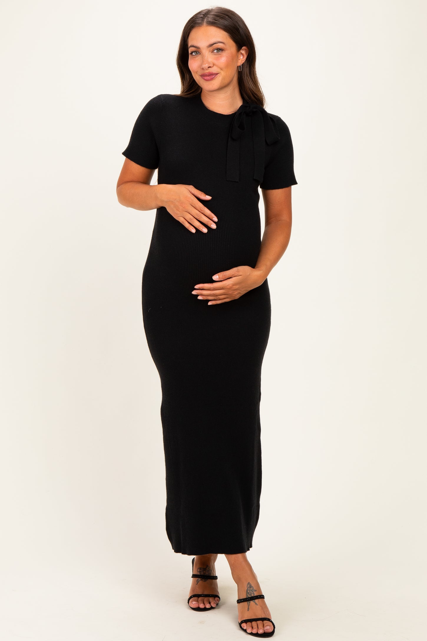 woman wearing a black ribbed maternity dress with a bow detail, holding her baby bump