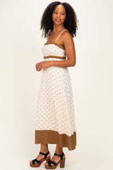 woman wearing a cream polka dot crop top and matching midi skirt with brown trim, standing sideways with curly hair