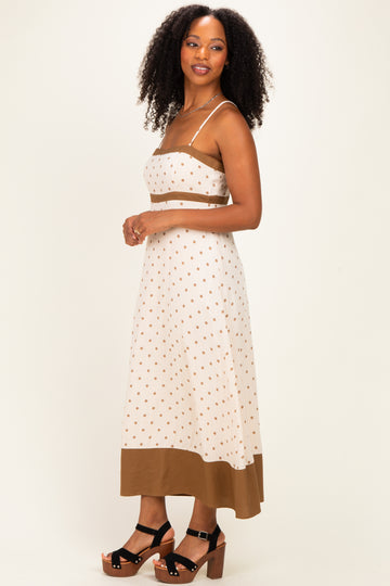 woman wearing a cream polka dot crop top and matching midi skirt with brown trim, standing sideways with curly hair