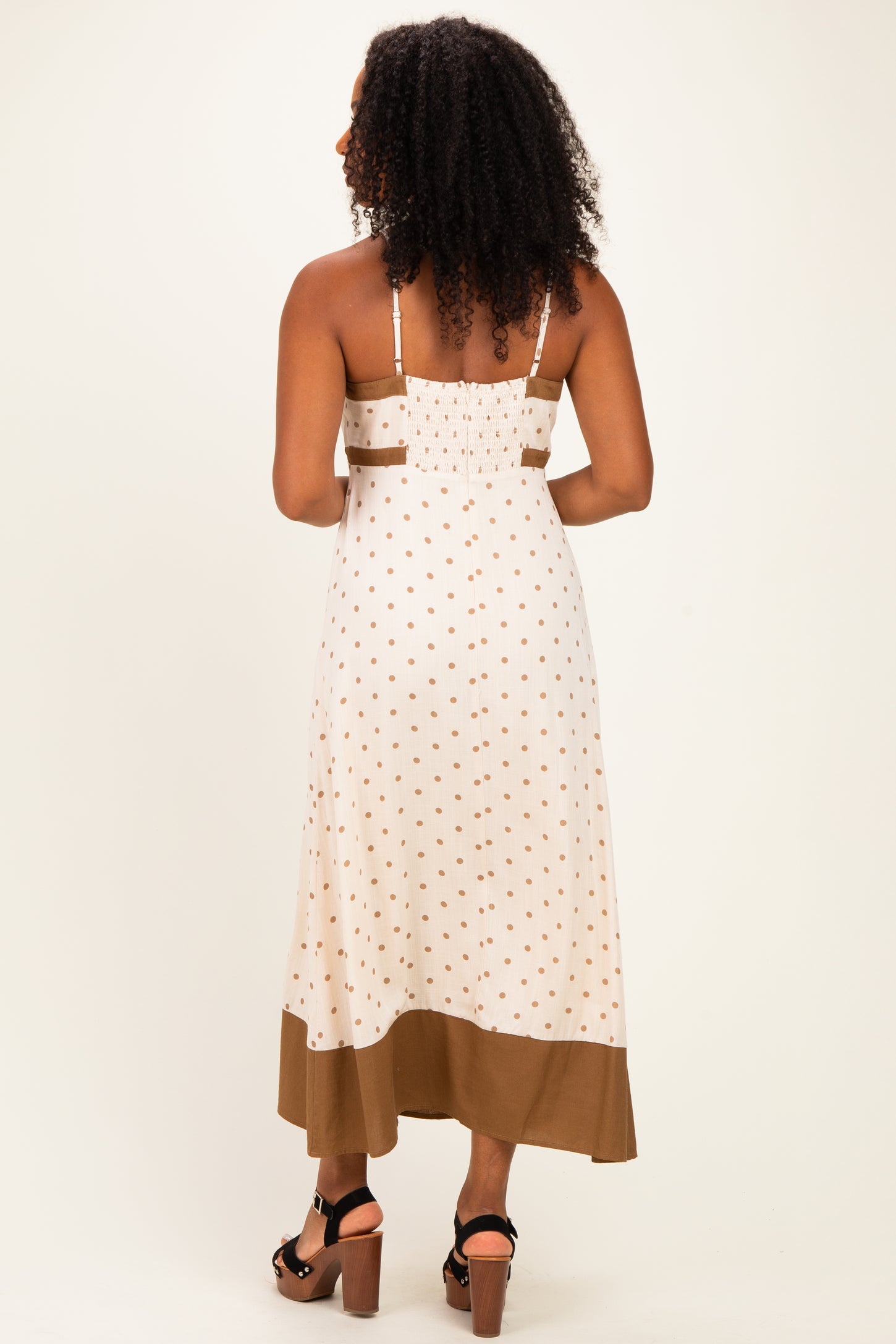 woman wearing a white midi dress with brown polka dots and a brown bottom hem, showing the back view