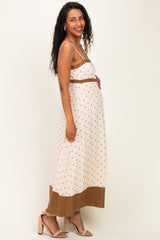 woman wearing a cream maternity maxi dress with brown polka dots and a solid brown hem, showing her baby bump