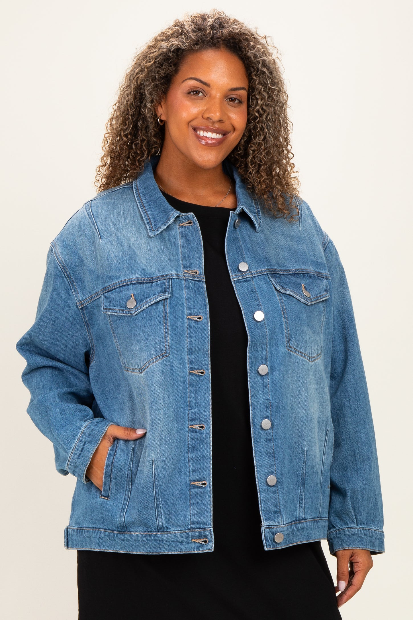 woman wearing a light wash oversized denim jacket with pockets and buttoned front over a black dress