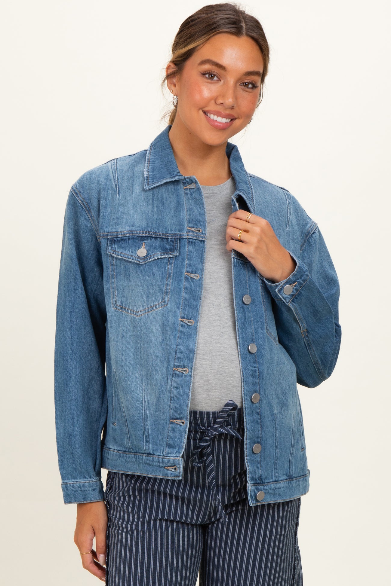woman wearing a light blue maternity denim jacket over a gray top with a relaxed fit, smiling and posing