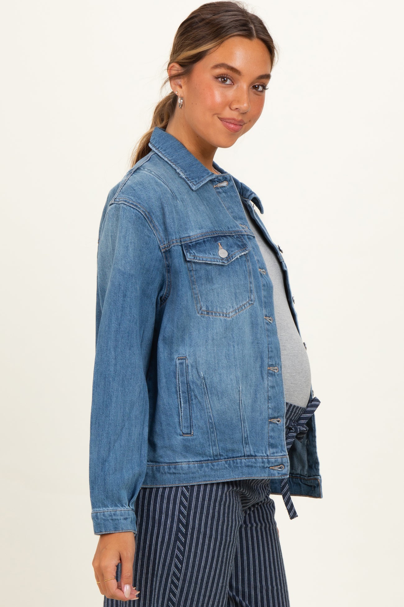woman wearing a light blue denim maternity jacket over a gray top, with a visible baby bump, facing sideways