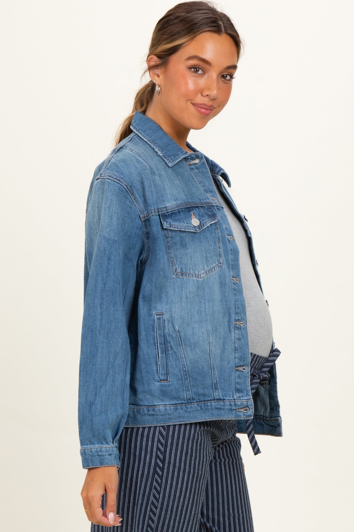 woman wearing a light blue denim maternity jacket over a gray top, with a visible baby bump, facing sideways