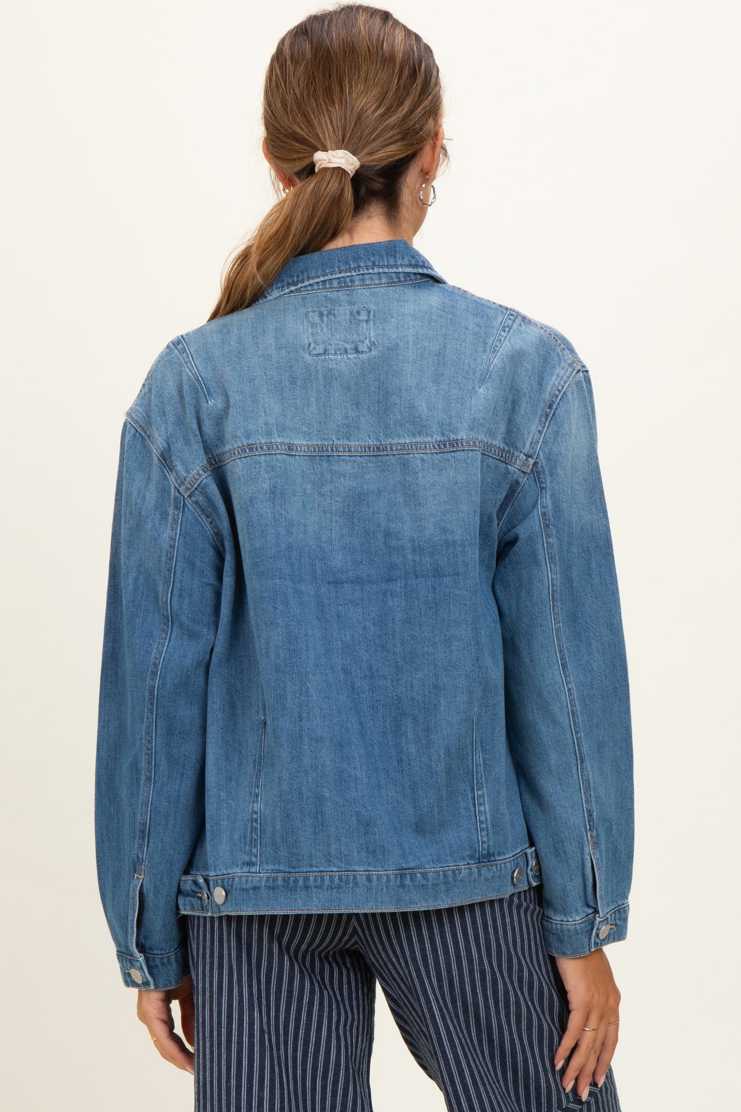 woman wearing a light blue denim maternity jacket, seen from the back with long sleeves and relaxed fit
