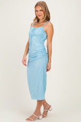 woman wearing a light blue midi dress with ruching details and thin straps, posing sideways against a neutral background
