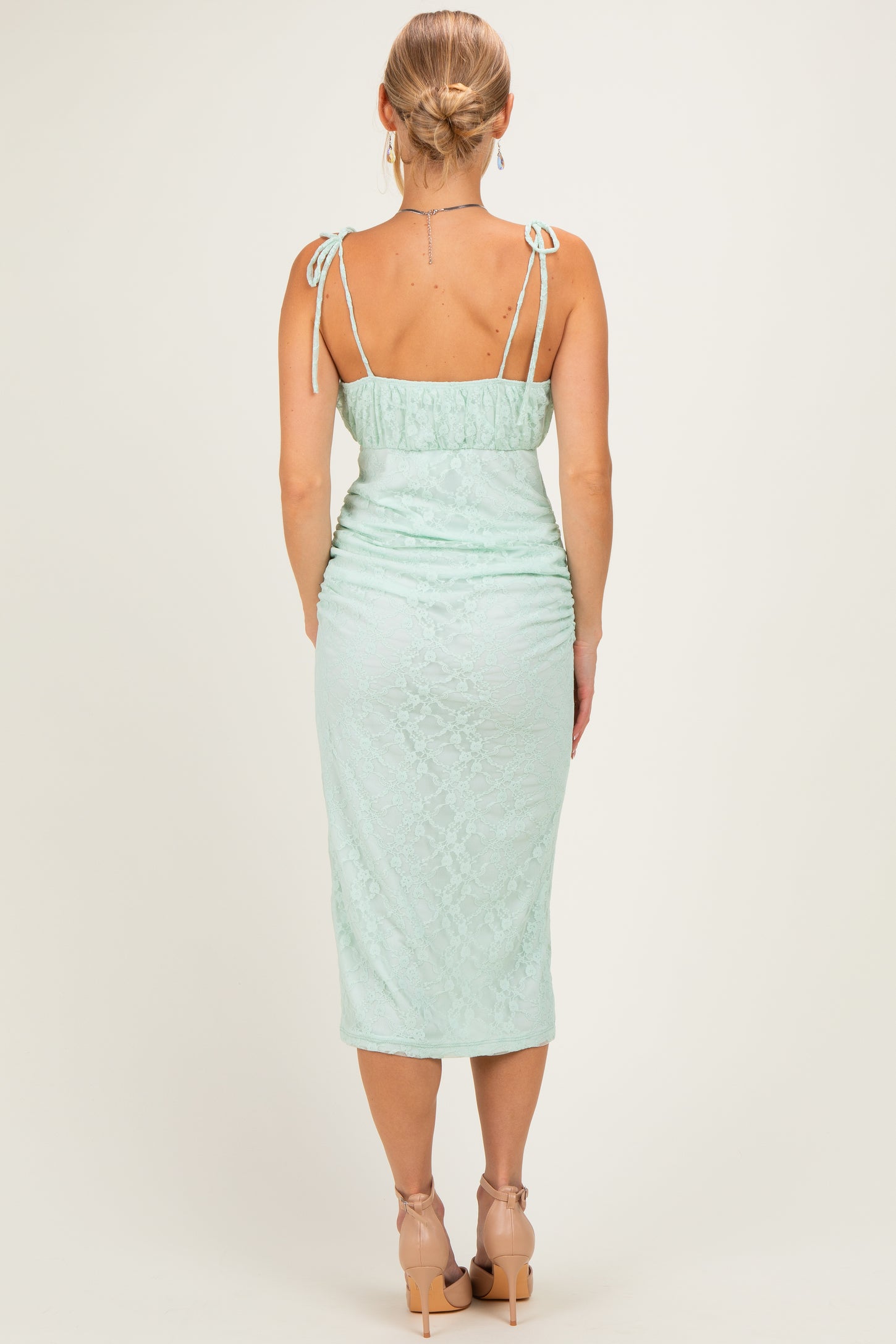 woman wearing a mint green fitted midi dress with lace detailing and adjustable tie straps, seen from the back