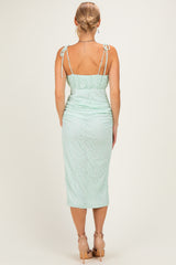 woman wearing a mint green fitted midi dress with lace detailing and adjustable tie straps, seen from the back