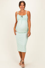 woman wearing a light green maternity dress with adjustable straps and a fitted silhouette, highlighting her baby bump