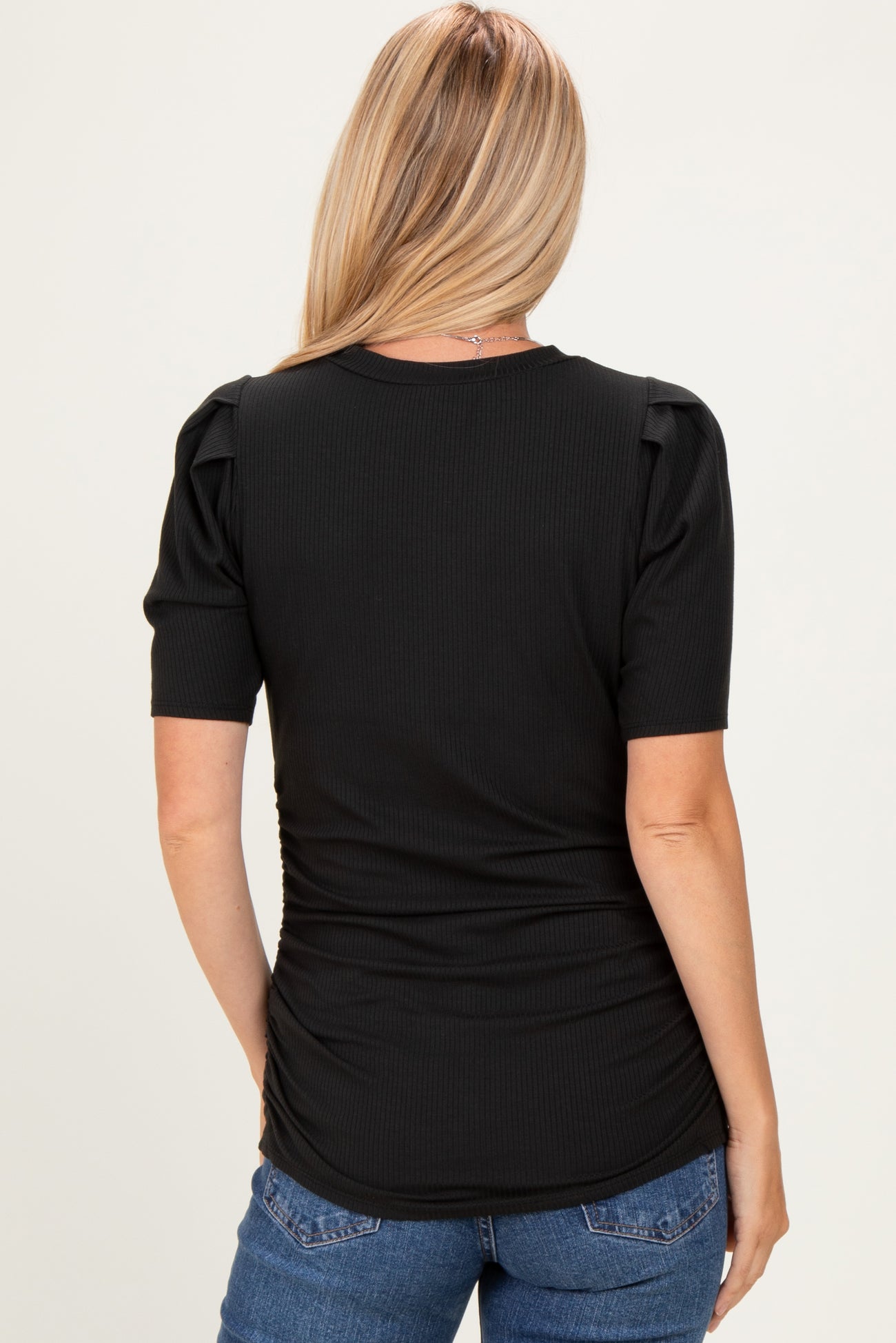 woman wearing a black ribbed top with puffed sleeves and gathered side detailing, seen from the back