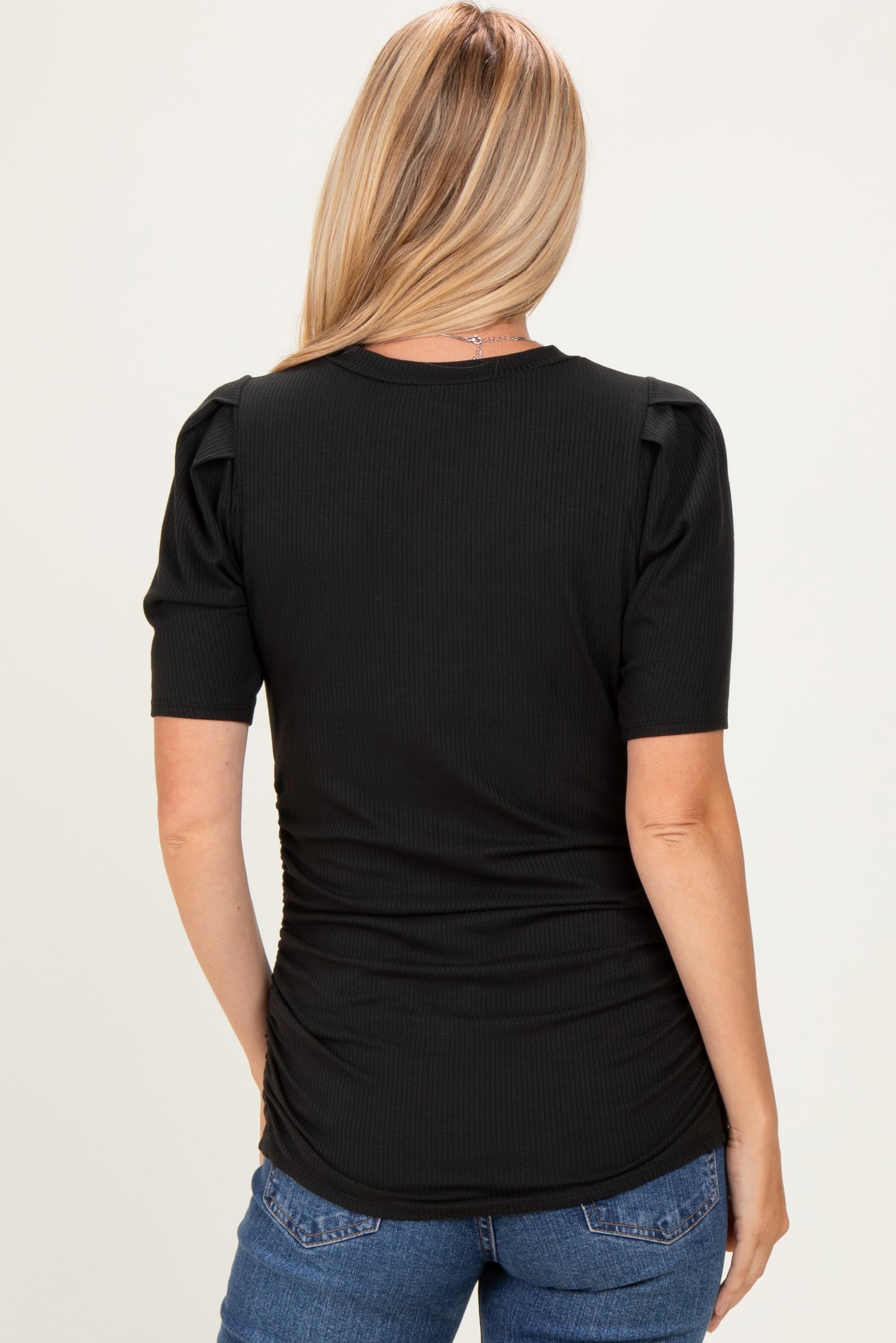 woman wearing a black ribbed top with puffed sleeves and gathered side detailing, seen from the back