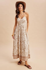 woman wearing a printed halter maxi dress with pockets and a straw hat, standing on a beige background
