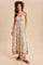 woman wearing a printed halter maxi dress with pockets and a straw hat, standing on a beige background