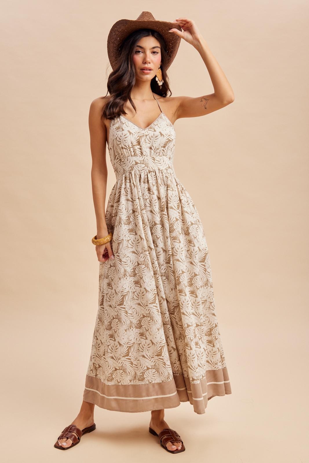 woman wearing a cream floral print maxi dress with a fitted bodice and flared skirt, accessorized with a hat and sandals