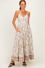 woman wearing a beige floral maxi dress with a halter neckline and pockets, standing and smiling