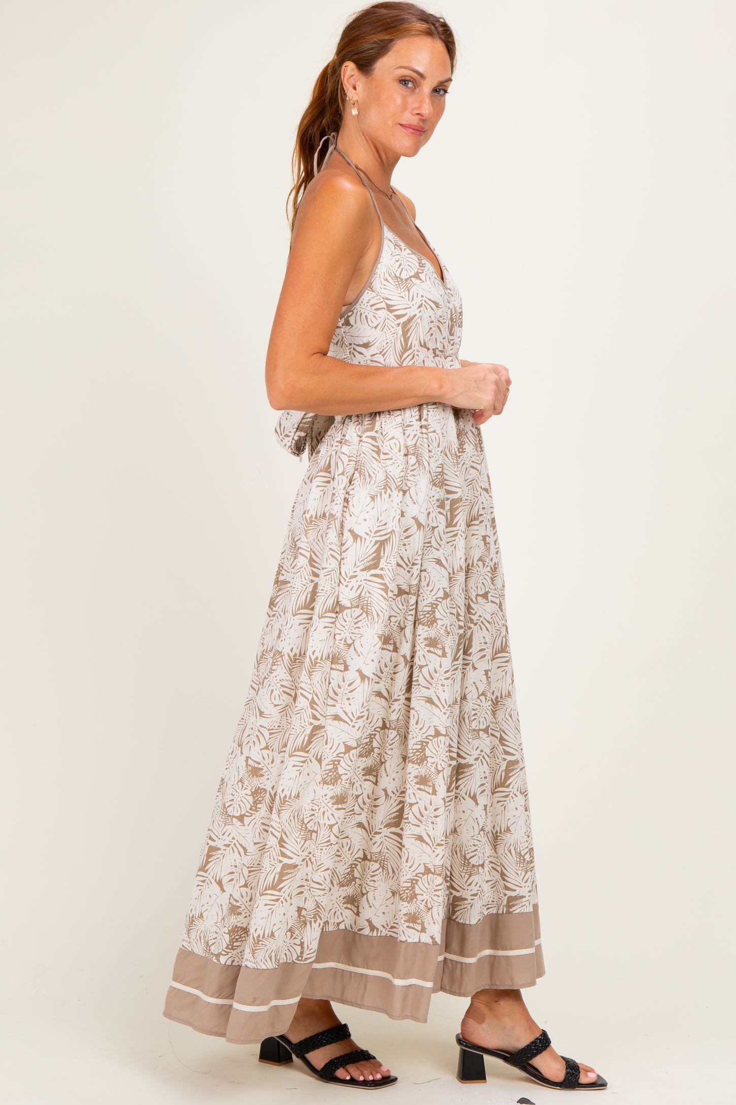 woman wearing a beige floral maxi dress with adjustable straps and a tiered hem, styled with black sandals