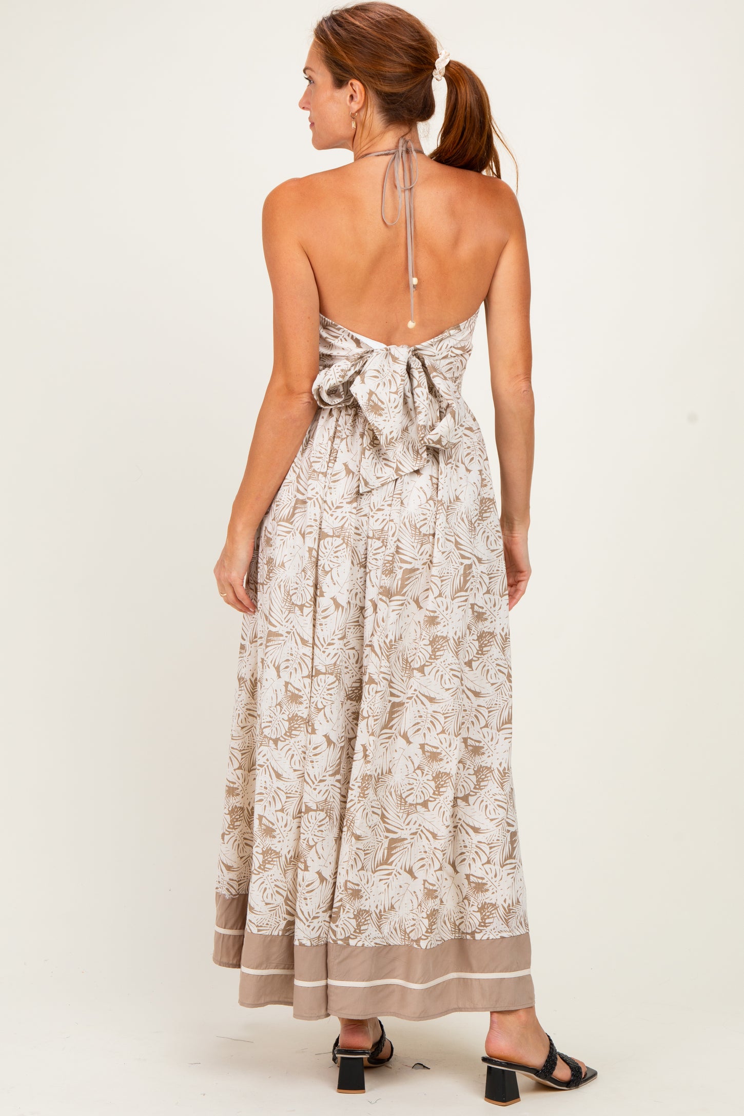 woman wearing a backless light brown floral maxi dress with a tie detail and a flared skirt