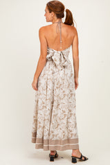 woman wearing a backless light brown floral maxi dress with a tie detail and a flared skirt