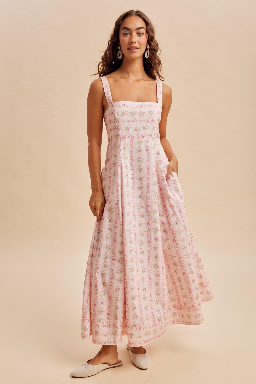 woman wearing a pink floral maxi dress with square neckline and pockets, standing on a neutral background