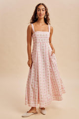woman wearing a pink floral maxi dress with square neckline and pockets, standing on a neutral background