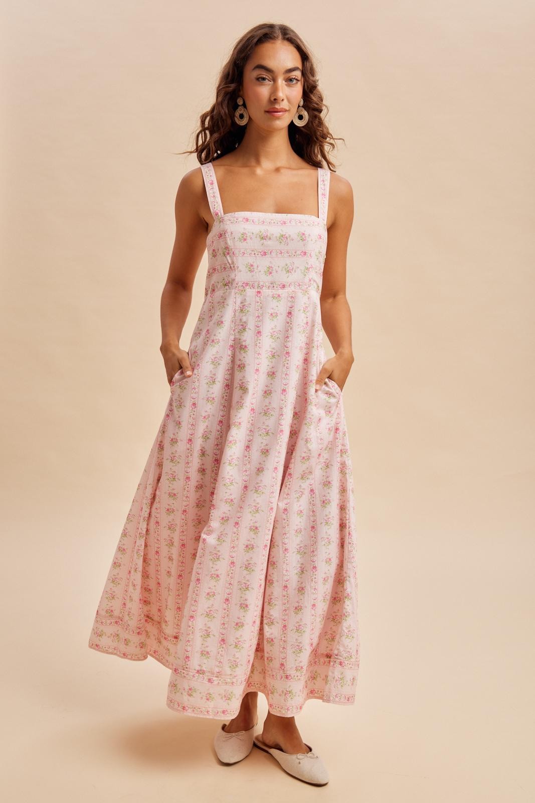 woman wearing a pink floral maxi dress with square neckline and pockets, set against a neutral background