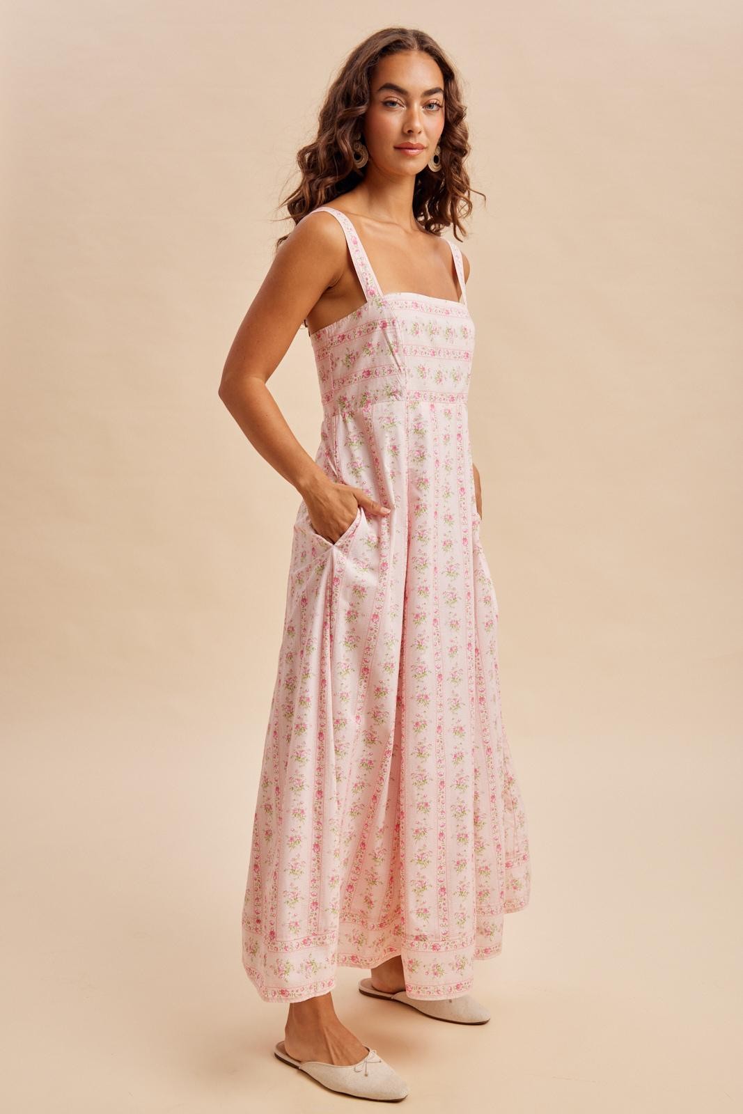 woman wearing a flowy pink floral maxi dress with slim straps and side pockets