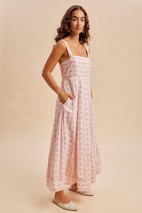 woman wearing a flowy pink floral maxi dress with slim straps and side pockets