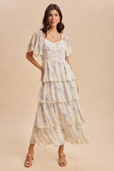 woman wearing a cream floral maxi dress with tiered layers and flutter sleeves