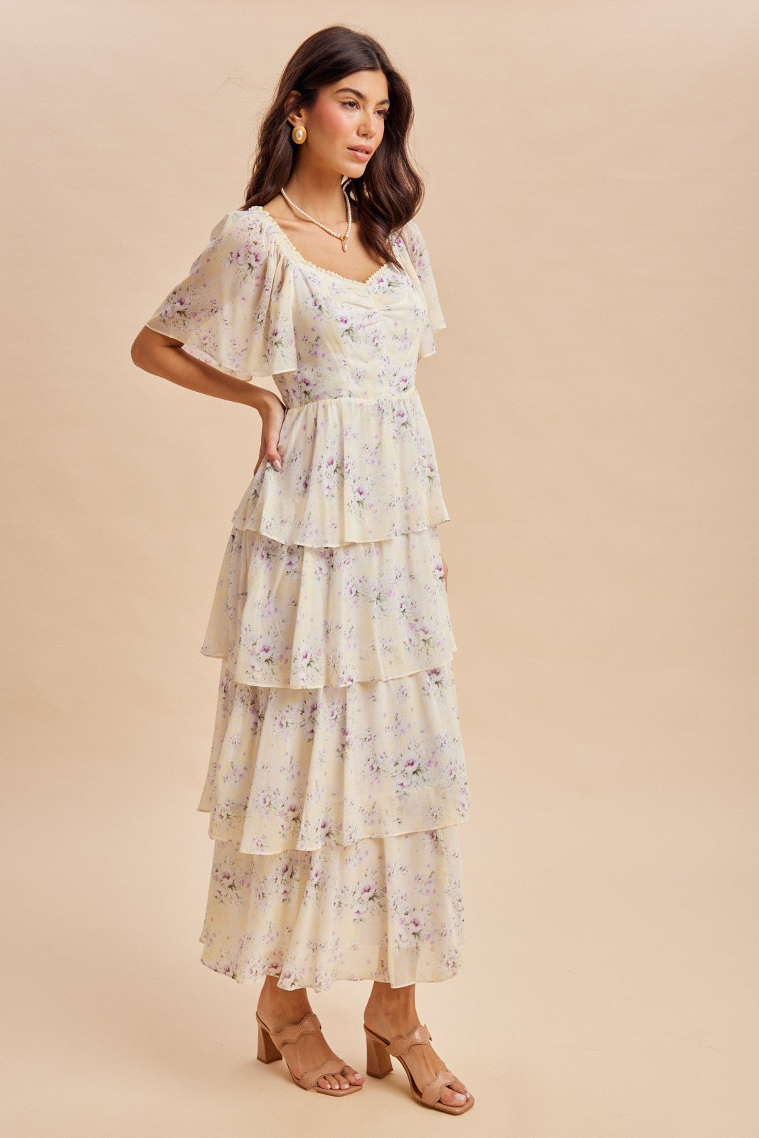 woman wearing a cream floral tiered maxi dress with short flutter sleeves and wooden heeled sandals