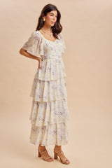 woman wearing a cream floral tiered maxi dress with short flutter sleeves and wooden heeled sandals