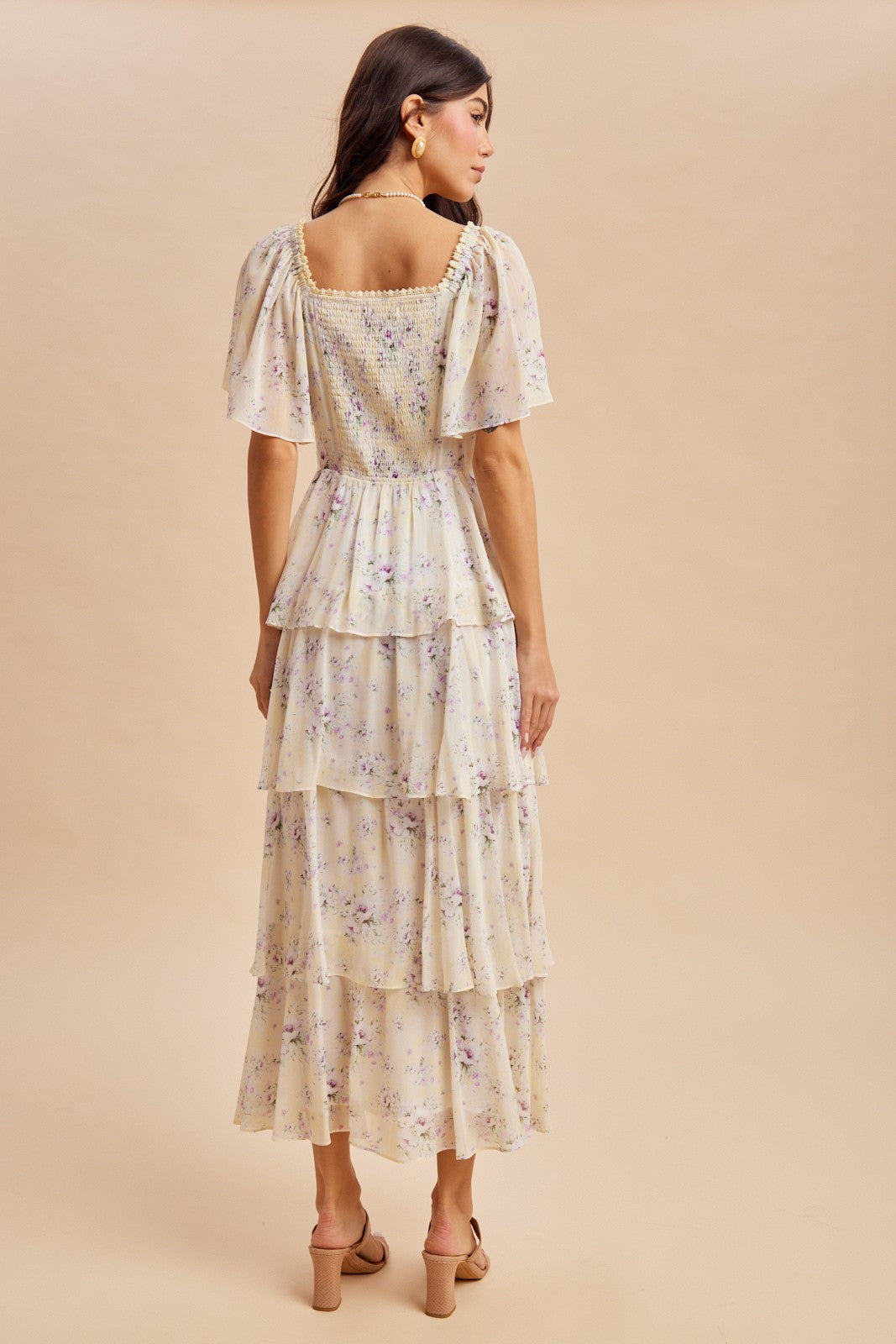 woman wearing a cream floral tiered maxi dress with puff sleeves, shown from the back