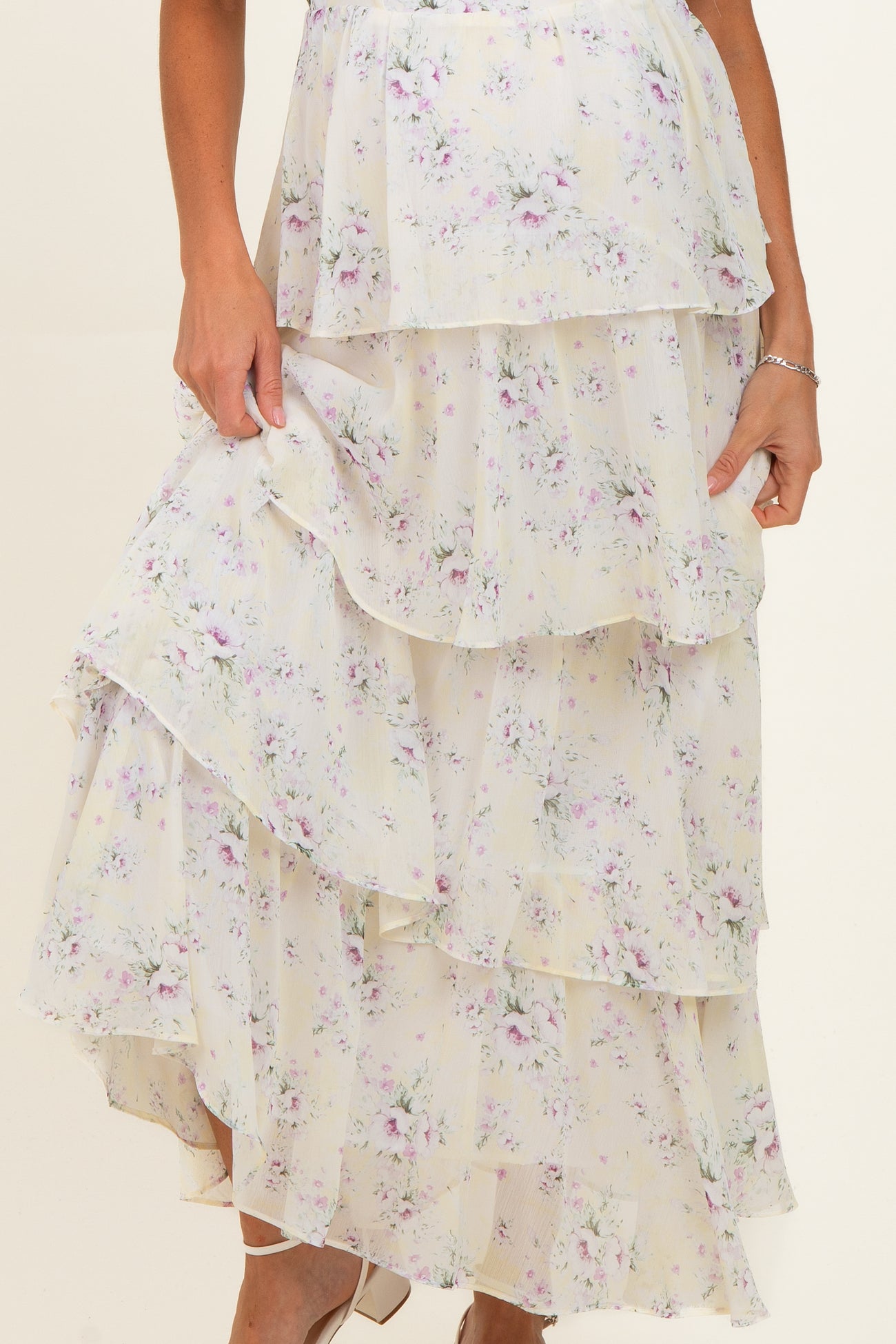 maternity wear floral tiered maxi dress in soft cream with purple and green accents, model holding the skirt hem