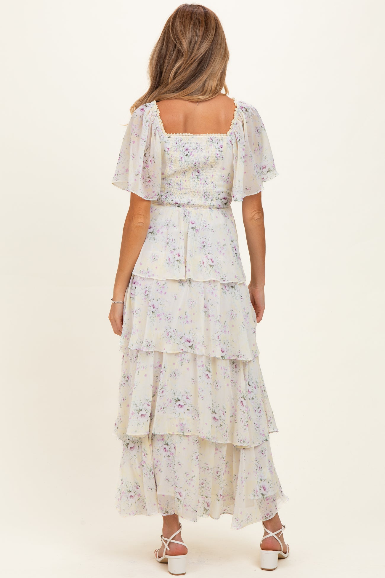 woman wearing a floral printed maternity maxi dress with tiered ruffles and short flutter sleeves, showing a baby bump